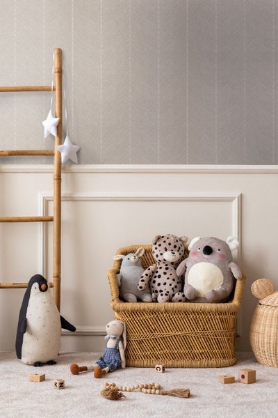 Vliestapete mit feinem Fischgrätmuster im Kinderzimmer über einer weißen Wandvertäfelung mit Kuscheltieren und Rattanmöbeln.