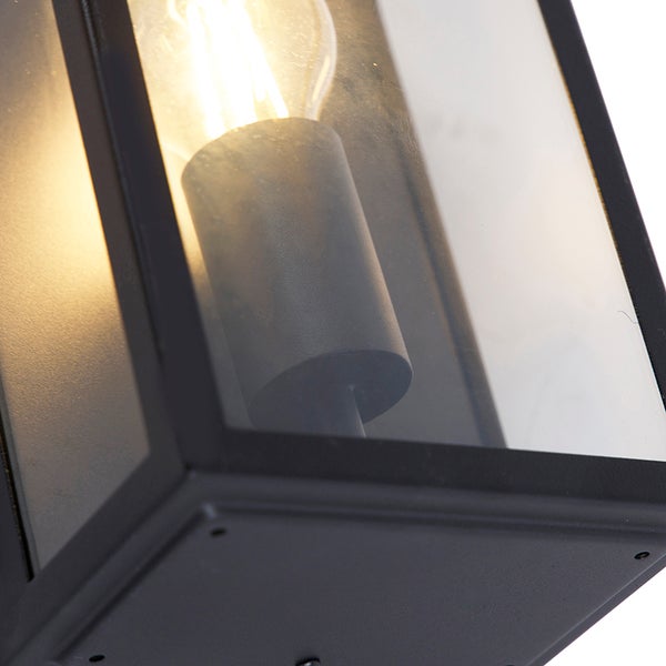 Nahaufnahme einer schwarzen Außenwandleuchte im Laternen-Stil aus Metall und Glas mit leuchtender Filamentlampe.