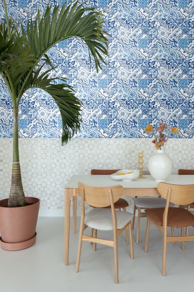 Esszimmer mit Esstisch, Stühlen, Pflanze im Topf und Fliesenmuster an der Wand.