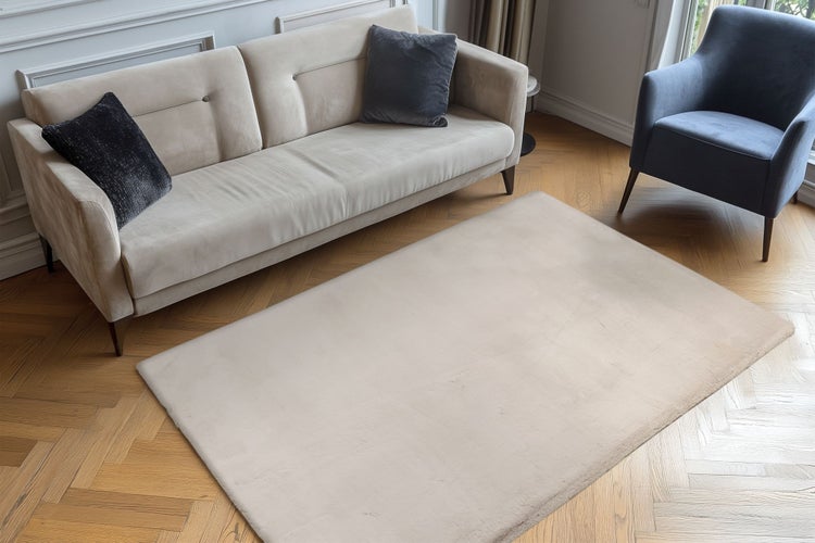 Ein unifarbener Teppich vor einem Sofa und einem Sessel in einem Wohnzimmer mit Fischgrätparkett.