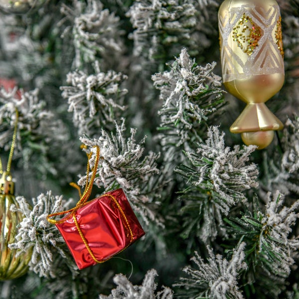 Schneebedeckter künstlicher Weihnachtsbaum mit einem kleinen roten Geschenk-Anhänger und einer goldenen gemusterten Christbaumkugel.