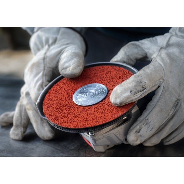 Eine Schleifscheibe mit X-Lock Aufnahme wird von zwei behandschuhten Händen gehalten.