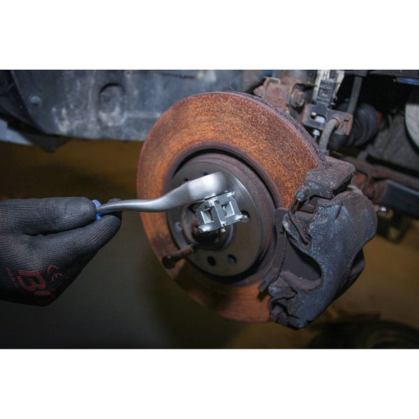 Hand mit Handschuh hält einen Wellenmutter-Schlüssel an einer Autoradaufhängung mit Bremsscheibe.