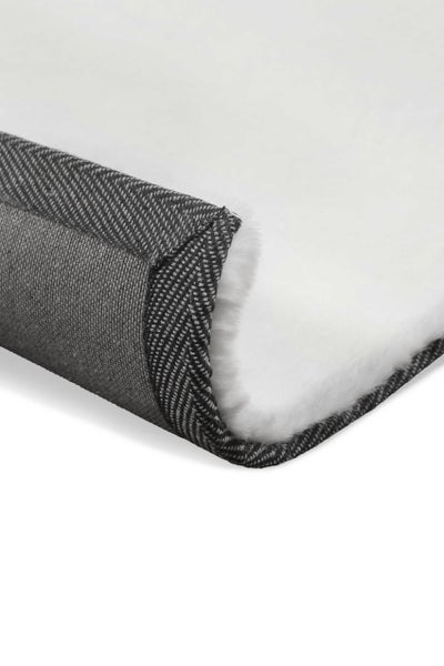 Nahaufnahme eines weißen Kunstfellteppichs mit grauer Rückseite im Fischgrätmuster und weicher Oberfläche.
