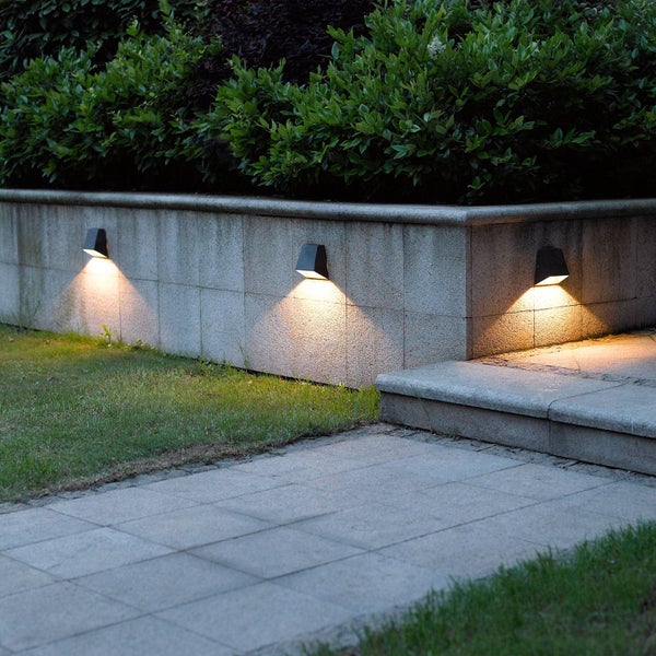Drei moderne Außenwandleuchten an einer Steinmauer, die einen Gartenweg mit warmem Licht beleuchten.