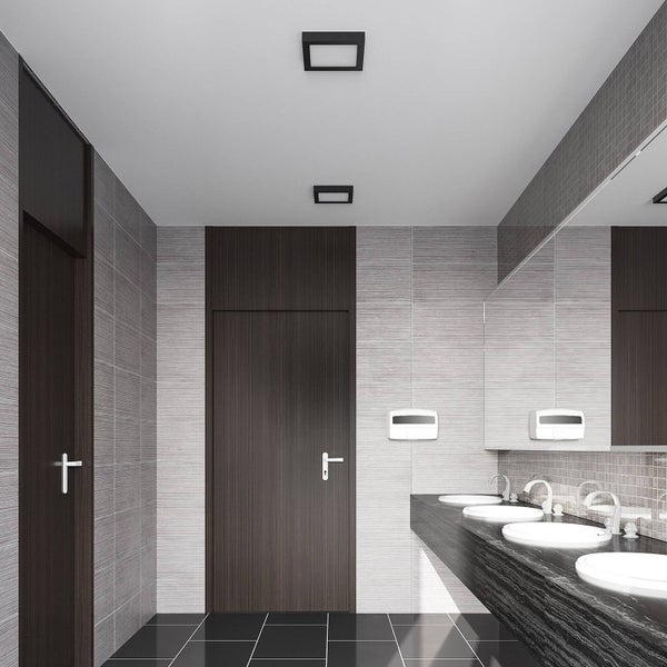 Modernes Badezimmer mit dunklen Holztüren, grauen Wandfliesen, schwarzem Waschtisch mit vier weißen Waschbecken und quadratischen Deckenleuchten.