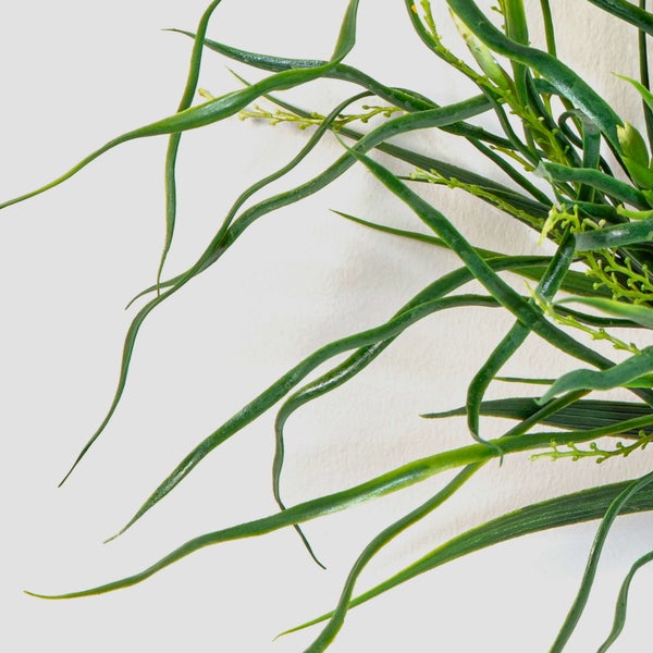 Künstliche Pflanze mit langen, wellenförmigen grünen Blättern.