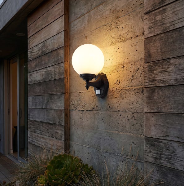 Außenwandleuchte mit kugelförmigem Glasschirm und schwarzer Halterung inklusive Bewegungsmelder, montiert an einer Wand aus Beton und Holz.