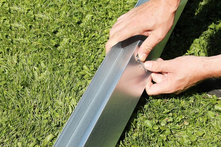 Eine Person befestigt einen Metallzaunpfosten mit einer Klammer