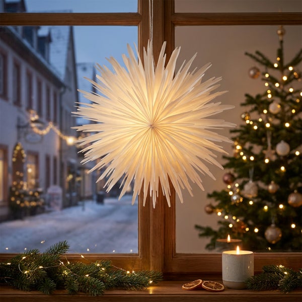Beleuchteter Papierstern als Fensterdekoration in einer weihnachtlich dekorierten Wohnung mit Tannenbaum und Kerze vor einem winterlichen Ausblick.