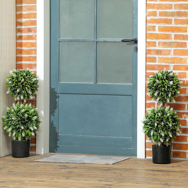 Dekorative Eingangsszene mit Tür, Fußmatte und Kunstpflanzen in Töpfen.