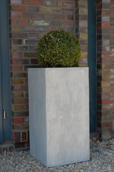 Hoher rechteckiger Pflanzkübel in Betonoptik mit einer Buchsbaumkugel vor einer Ziegelwand im Außenbereich.