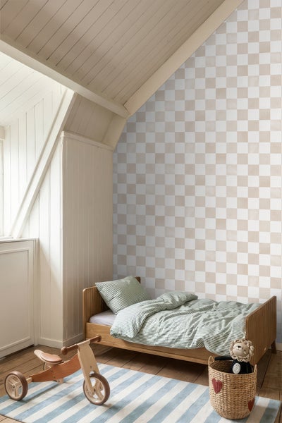 Kinderzimmer mit karierter Tapete in Beige und Weiß, einem Holzbett mit gestreifter Bettwäsche und einem Holzdreirad unter einer Dachschräge.