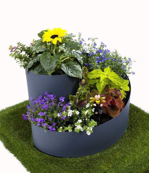 Anthrazitfarbene Pflanzspirale aus Kunststoff, bepflanzt mit bunten Blumen wie Sonnenblumen und Lobelien auf einer Rasenfläche.