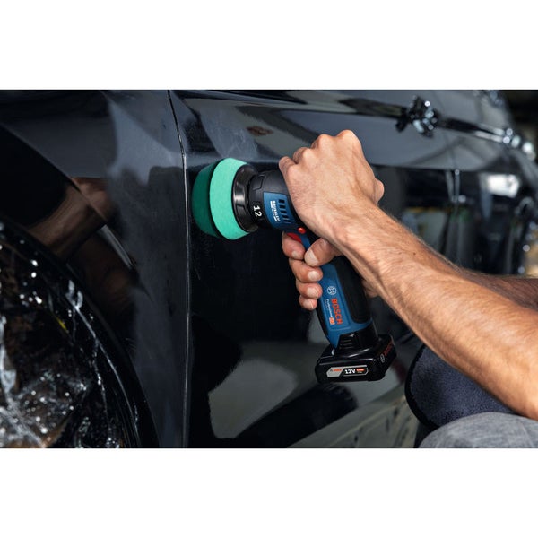 Ein Handwerker arbeitet mit einer Poliermaschine an einem Auto in einer Werkstatt.