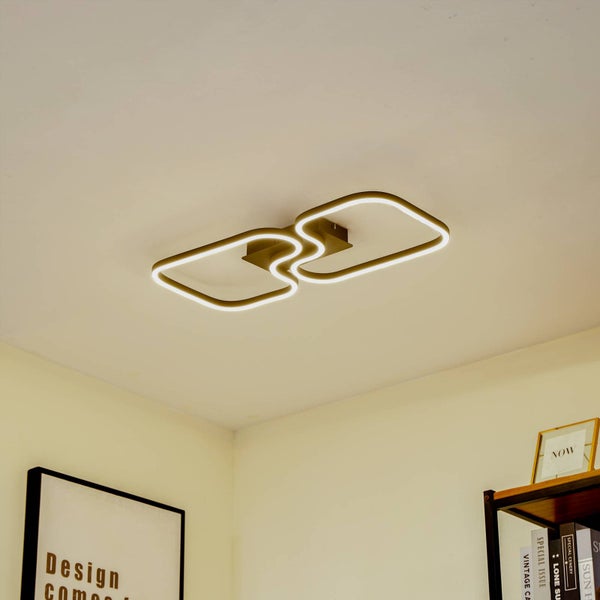 Moderne LED-Deckenleuchte mit zwei verbundenen, abgerundeten quadratischen Lichtelementen an einer weißen Decke in einem hellen Wohnraum.