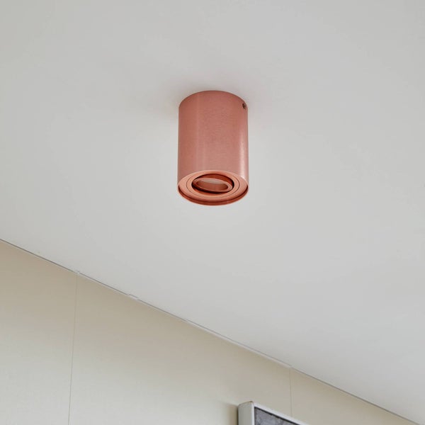 Zylindrischer Aufbaustrahler aus Metall in Kupferoptik an einer Decke montiert.