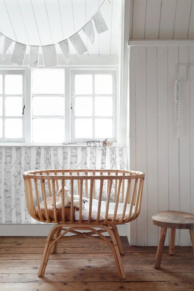 Helles Kinderzimmer mit Babywiege aus Rattan, Dekoration und Holzhocker