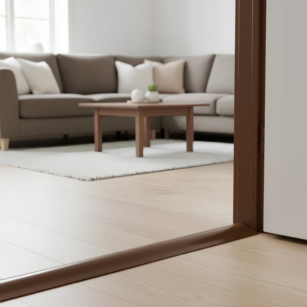 Eine braune Türschwelle aus Metall installiert in einem modernen Wohnzimmer mit hellem Parkettboden und einem Sofa im Hintergrund.