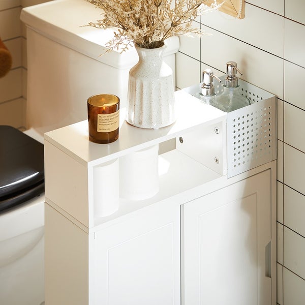 Weißer Badschrank neben einer Toilette mit Kerze, Vase, Seifenspender und Toilettenpapier