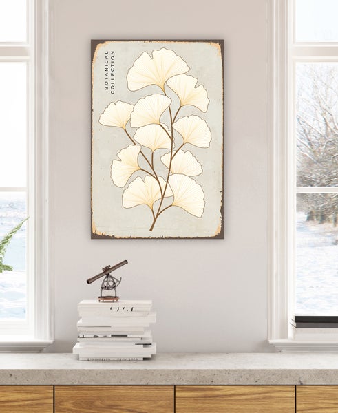 Wandbild mit Ginkgo-Motiv im Vintage-Stil über einer Anrichte mit Büchern in einer hellen, modern eingerichteten Wohnumgebung.
