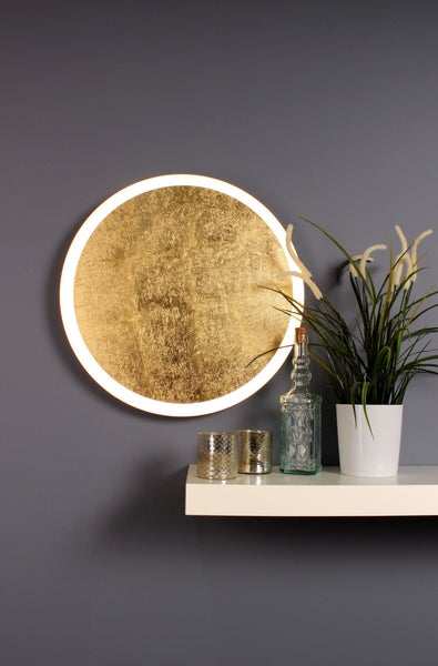 Runde Wandleuchte in Goldoptik mit leuchtendem Ring, montiert über einem weißen Regal mit Dekoration.