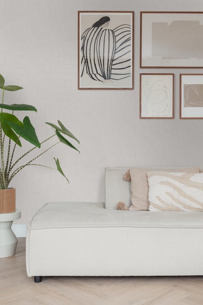 Helles Wohnzimmer mit Couch, Kissen, Pflanzen und Bildern an der Wand