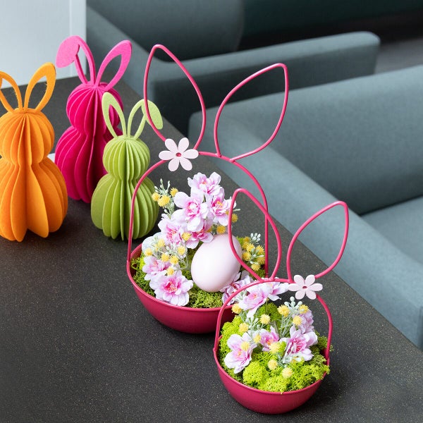 Osterdekoration bestehend aus Filzhasen und Metallkörben mit künstlichen Blumen und Ostereiern als festliche Tischdekoration für Ostern