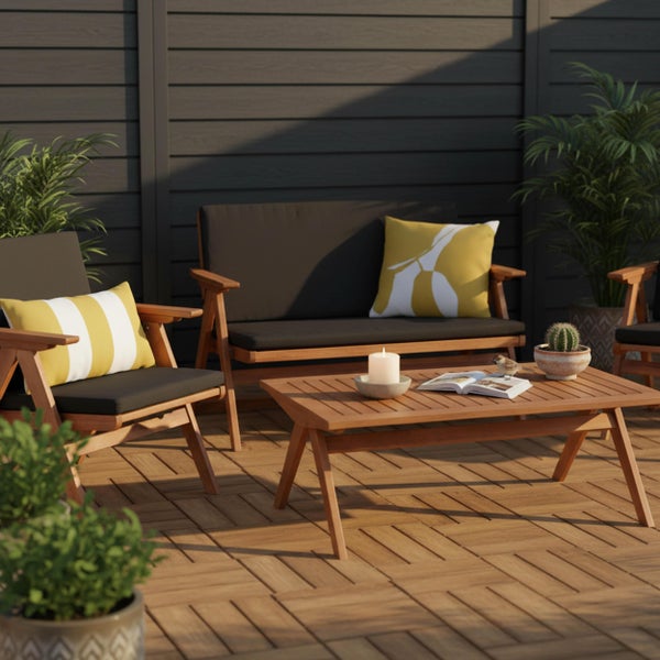 Gartenmöbel-Set aus Holz mit Sofa, Sessel und Couchtisch auf einer Holzterrasse vor einem dunklen Sichtschutzzaun.