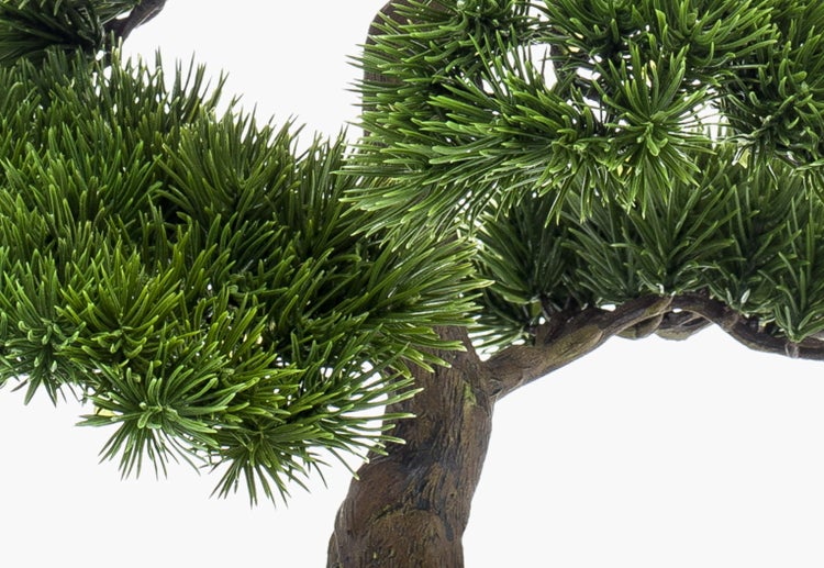Detailaufnahme eines künstlichen Bonsai-Baums mit grünen Nadeln und strukturiertem braunem Stamm.