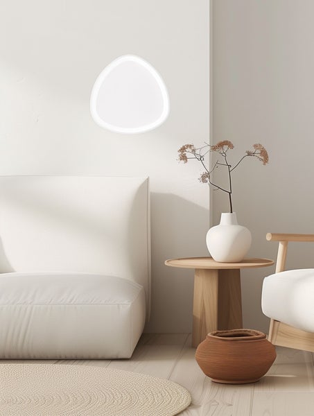 Moderne LED-Wandleuchte in organischer Form in einem hellen, minimalistischen Wohnzimmer mit Sofa und Holzbeistelltisch.