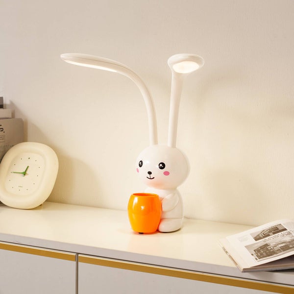 LED Schreibtischlampe in Hasenform mit integriertem Stiftehalter auf hellem Möbelstück, kindgerechtes Design mit zwei flexiblen Leuchtköpfen.