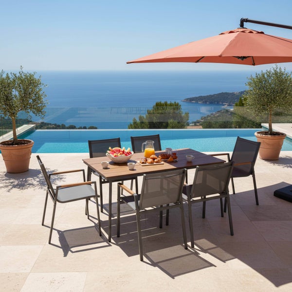 Gartenmöbel-Set mit Holztisch und grauen Stühlen auf einer hellen Terrasse mit Pool, Sonnenschirm und weitem Meerblick.