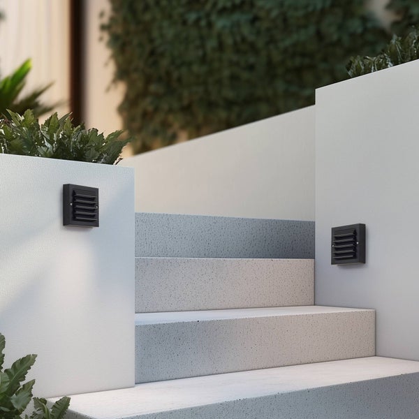 Zwei quadratische schwarze Außenwandleuchten mit Lamellen an weißen Mauern neben einer Steintreppe im Außenbereich.
