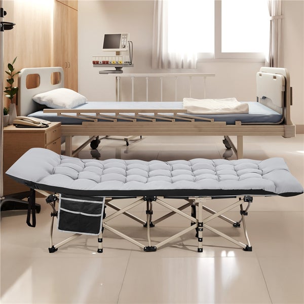 Gepolstertes graues Klappbett mit Metallrahmen in einem hellen Krankenzimmer neben einem Patientenbett.