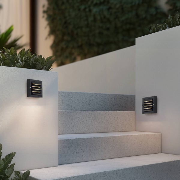 Schwarze quadratische Außenwandleuchten mit Lamellen an weißen Steinwänden zur Beleuchtung einer Außentreppe.