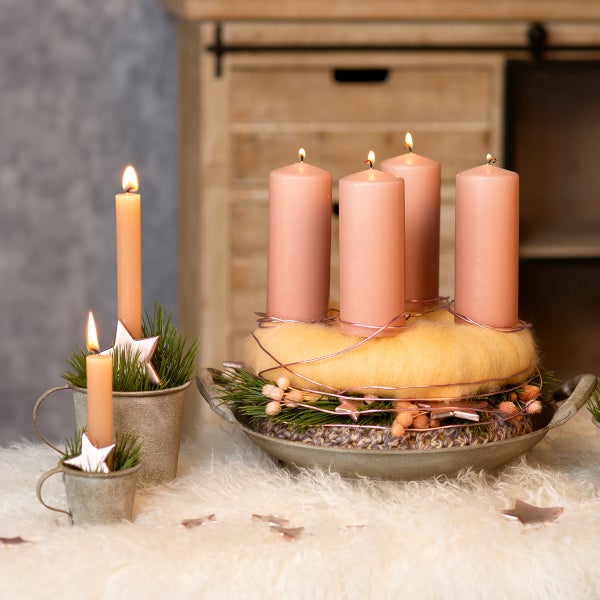 Adventskranz mit vier rosa Stumpenkerzen auf einer Metallschale mit Wollring und Tannenzweigen in festlich dekorierter, heller Umgebung.