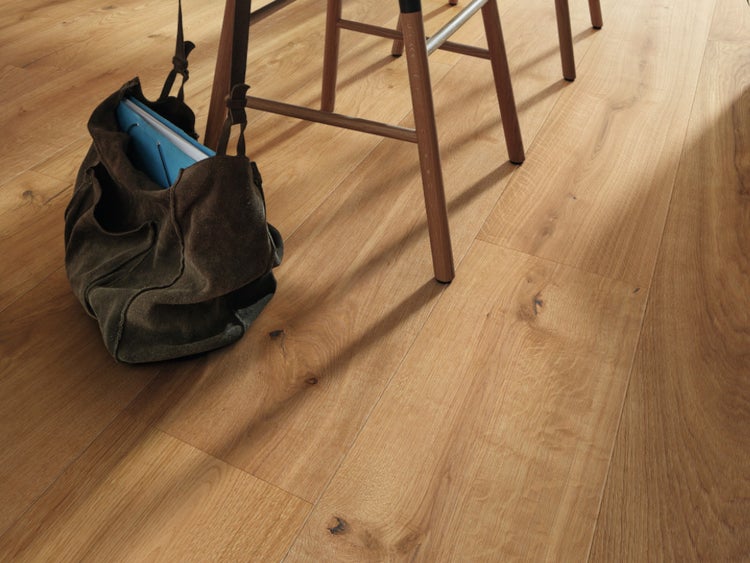 Parkettboden aus Landhausdielen in Eiche mit natürlicher Maserung und sichtbaren Ästen, abgebildet mit Holzhocker und Tasche.