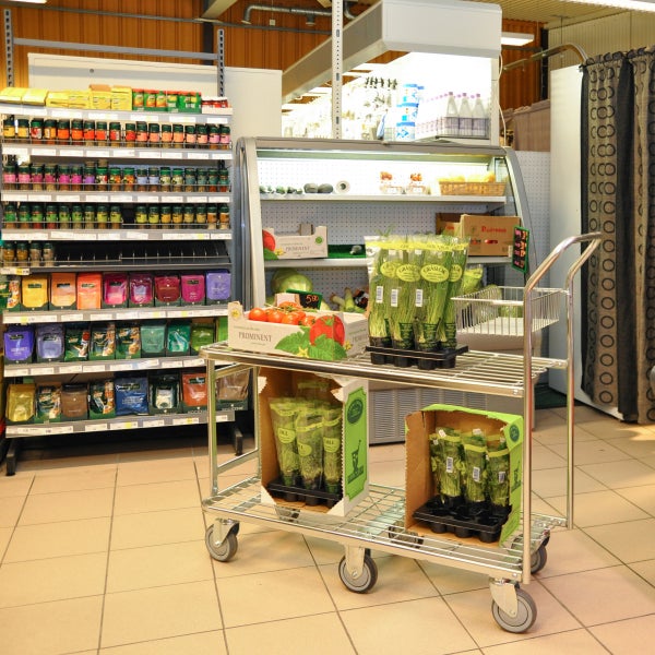 Verkaufsraum mit Gewürzregal, Kühlregal und Einkaufswagen mit Kräutern und Tomaten