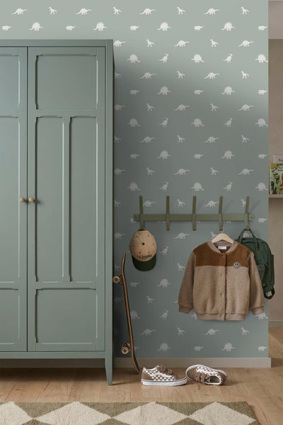 Vliestapete mit Dinosaurier-Muster in einem Kinderzimmer neben einem Schrank, einer Wandgarderobe mit Kleidung und einem Skateboard.