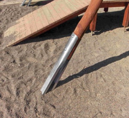Holzpfosten eines Spielgeräts mit Metallanker im Sand verankert, im Hintergrund eine Holzrampe.