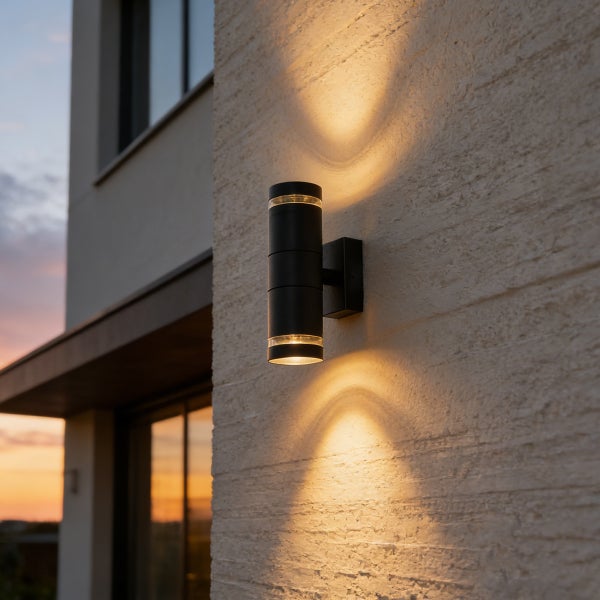 Moderne Außenwandleuchte in Schwarz an einer hellen Fassade mit Lichtkegel nach oben und unten bei Dämmerung.
