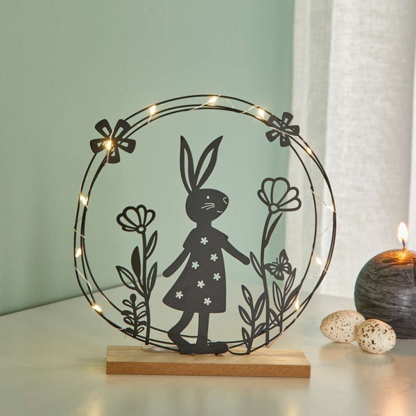 Dekorative Osterhasen-Silhouette mit Blumen und LED-Lichtern auf einem Holzsockel