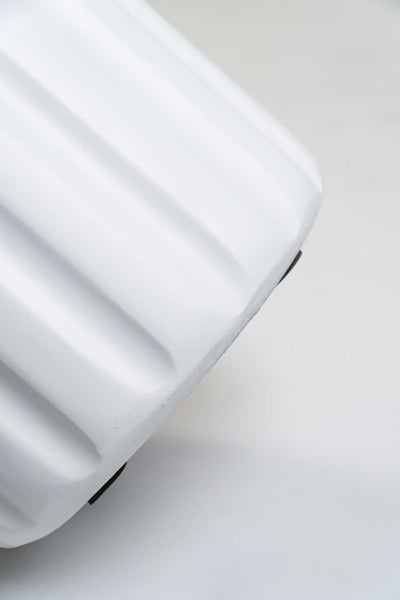 Nahaufnahme der geriffelten Oberfläche eines weißen Übertopfs mit Bodenschonern auf der Unterseite.