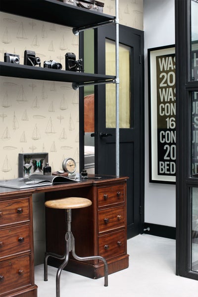 Vliestapete mit Segelboot-Muster in einem hellen Arbeitszimmer mit antikem Holzschreibtisch, Metallhocker und schwarzen Regalen.