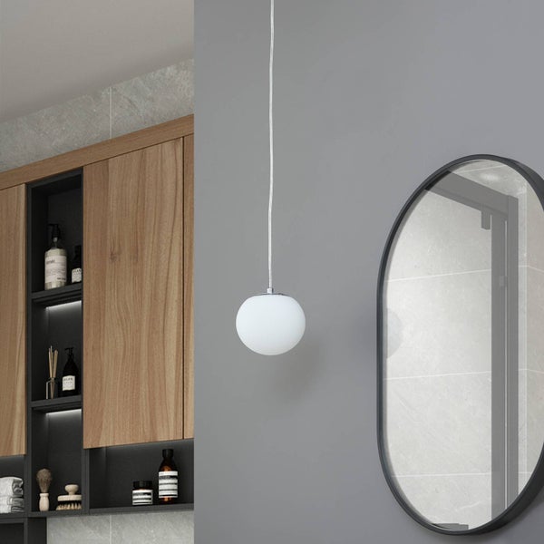 Runde Pendelleuchte aus weißem Glas in einem modernen Badezimmer mit Holzschränken und ovalem Spiegel an einer grauen Wand.