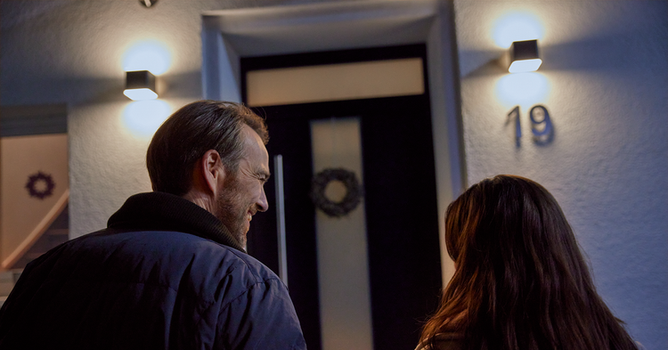 Mann und Frau vor einer Haustür mit zwei modernen Außenwandleuchten, die den Eingangsbereich bei Nacht hell beleuchten.