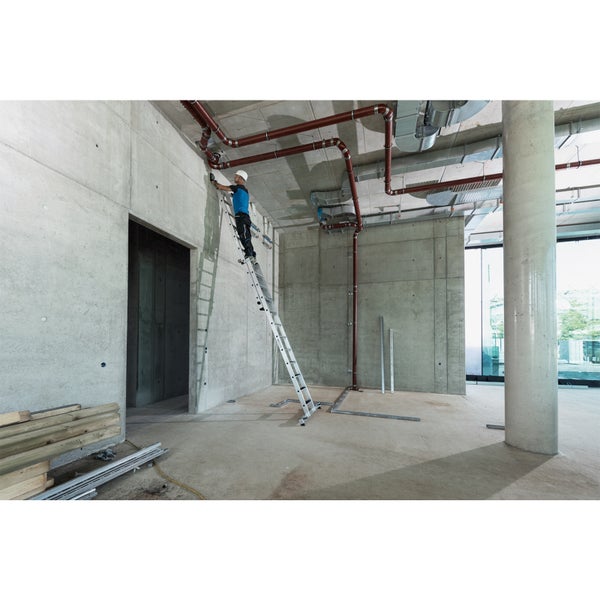 Handwerker auf einer Mehrzweckleiter bei Installationsarbeiten in einem Rohbau