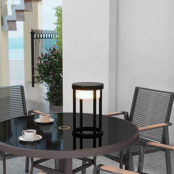 Schwarze Solar-Tischleuchte auf einem runden Tisch mit zwei Gartenstühlen auf einer hellen, modern gestalteten Terrasse.