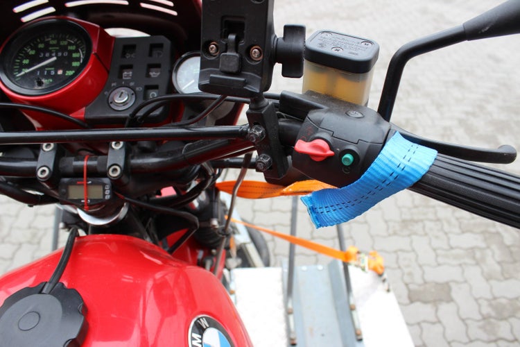 Detailansicht eines Motorradlenkers mit Zurrgurt zur Transportsicherung auf einer Ladefläche.